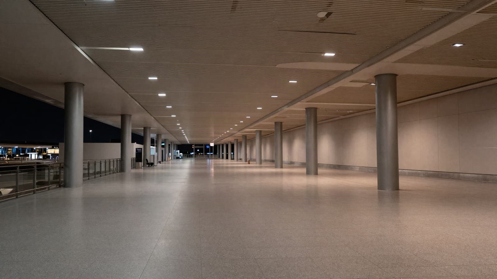 An empty airport concourse at night, receding to a vanishing point.